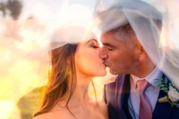 Bride and groom kissing under the veil at sunset in the orange grove at The Pavilion at Mixon Farms