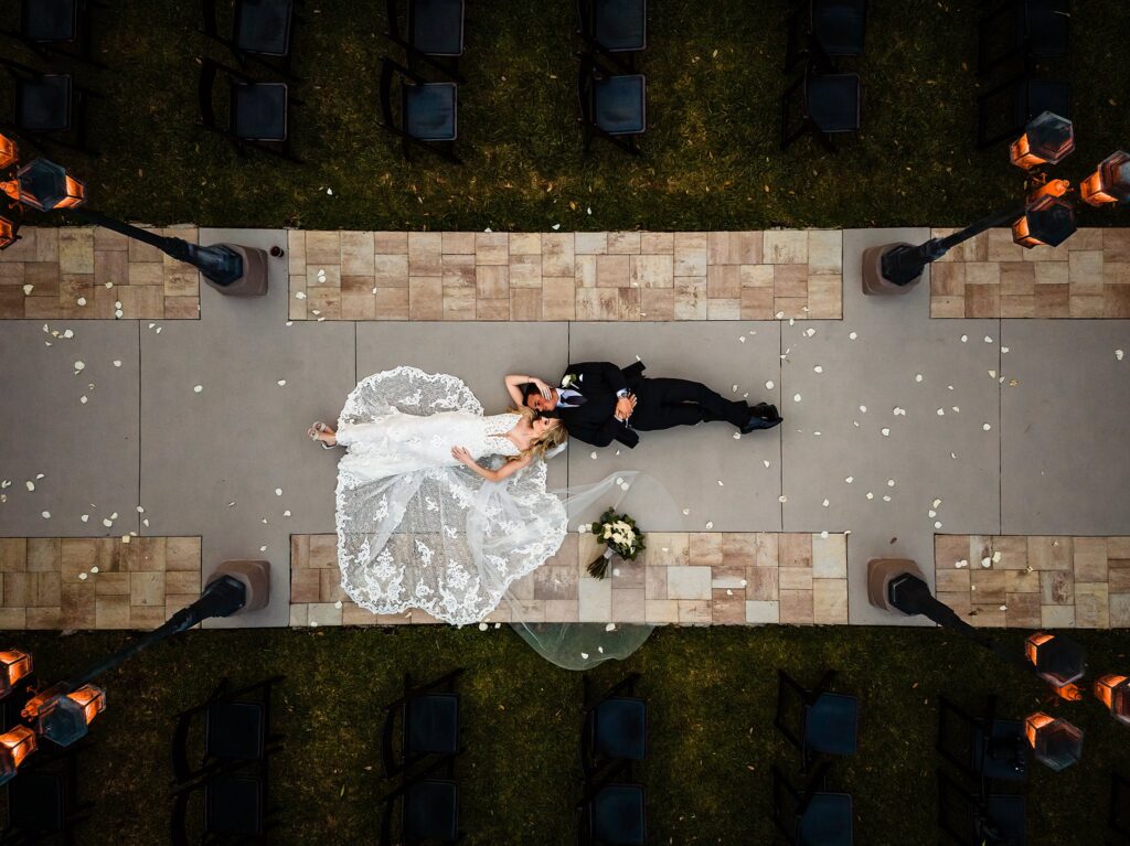 Drone shot of bride and groom lying on the pathway between Infinity Forest and Enchanted Garden Chapel at Bakers Ranch wedding venue in Parrish FL