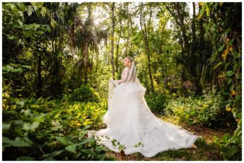 Bride in wedding gown and veil standing in the hidden wooded area at Bakers Ranch wedding venue in Parrish FL surrounded by natural Florida forest and palm trees