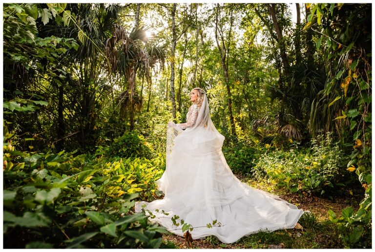 Bride in wedding gown and veil standing in the hidden wooded area at Bakers Ranch wedding venue in Parrish FL surrounded by natural Florida forest and palm trees