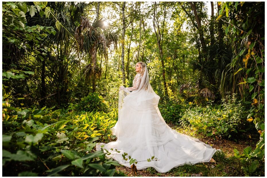 Bride in wedding gown and veil standing in the hidden wooded area at Bakers Ranch wedding venue in Parrish FL surrounded by natural Florida forest and palm trees