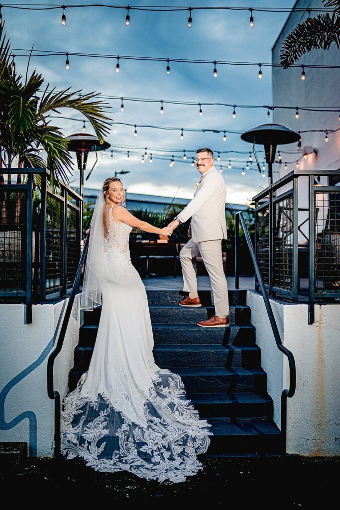 Becca and Logan on outdoor stairs patio string lights above at Urban Stillhouse wedding St Pete by Ying Multimedia
