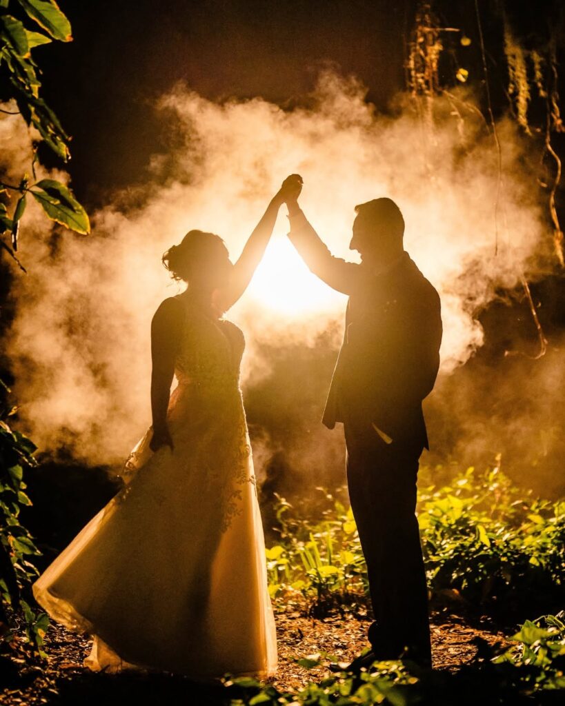 Silhouette of bride and groom dancing in the hidden wooded area at Bakers Ranch in Parrish FL with smoke and golden backlight at night