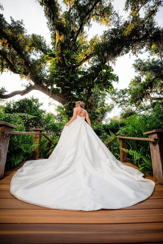Bride with cathedral train on the wooden Love Lock Bridge at Bakers Ranch wedding venue in Parrish FL surrounded by Spanish moss oak tree and lush ferns