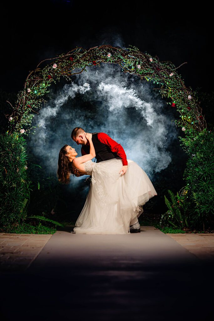Bride and groom dipping inside the Infinity Forest circular branch arch at Bakers Ranch wedding venue in Parrish FL at night with smoke machine and fairy lights