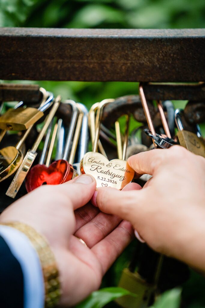 Bride and groom placing engraved heart shaped love lock on the fence at Love Lock Bridge at Bakers Ranch wedding venue in Parrish FL surrounded by other couples locks