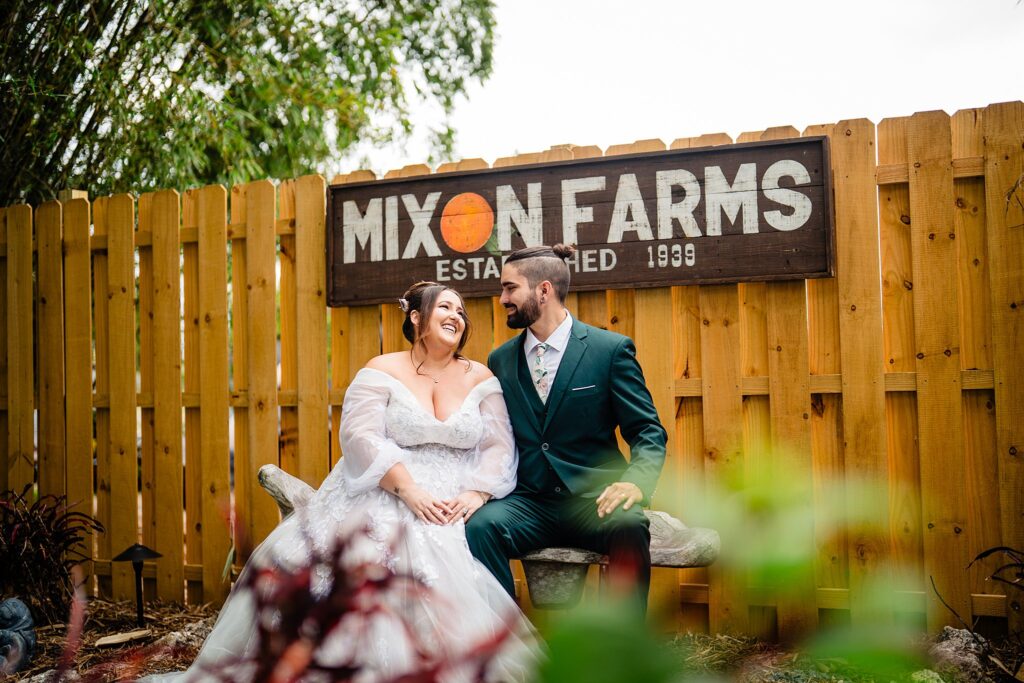 Bride and groom laughing together seated in front of the Mixon Farms established 1939 sign at The Pavilion at Mixon Farms, Bradenton Florida