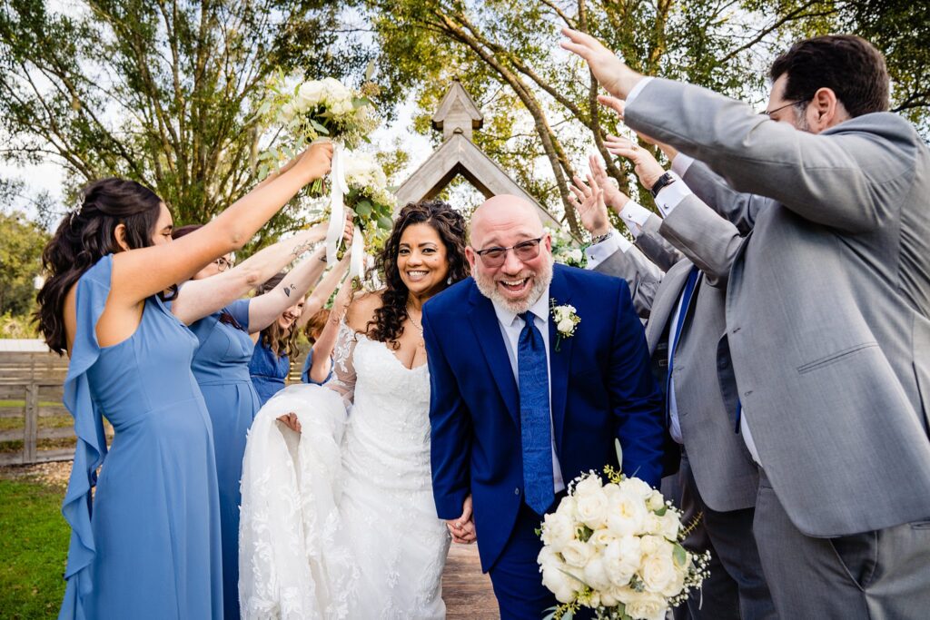 Bride and groom laughing and running through a tunnel of raised hands and bouquets created by the wedding party at Cow Creek Farm, Plant City Florida