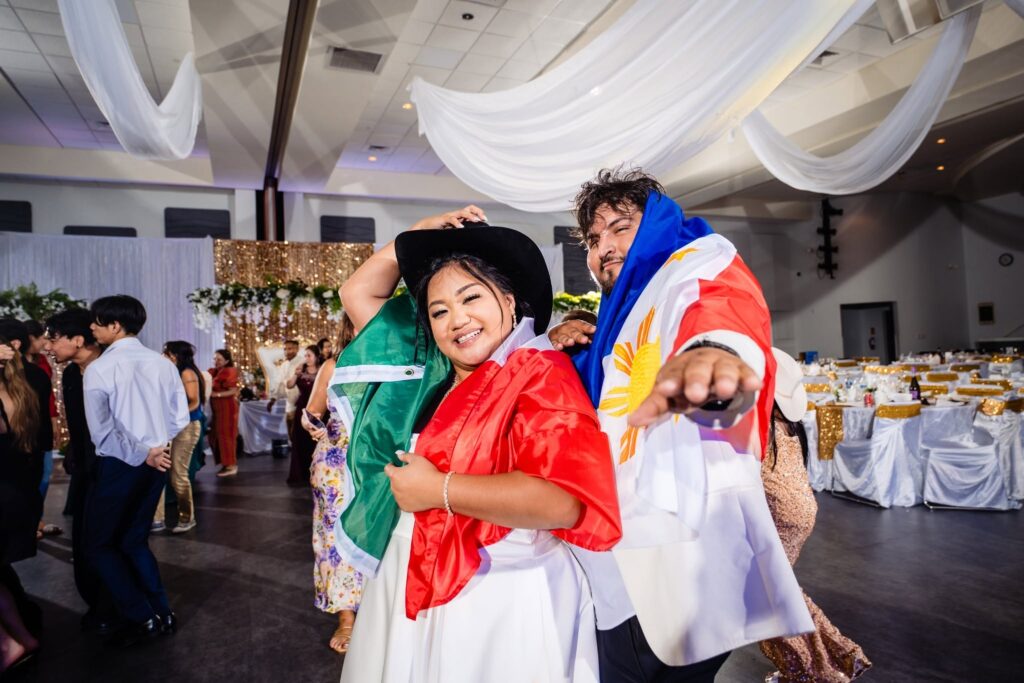 Bride draped in the Mexican flag and groom wrapped in the Philippine flag dancing together at their reception at the Venice Community Center, Florida wedding photographed by Ying Multimedia