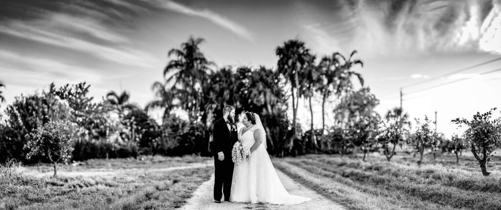 Bride and groom standing on a dirt path through the orange grove at The Pavilion at Mixon Farms