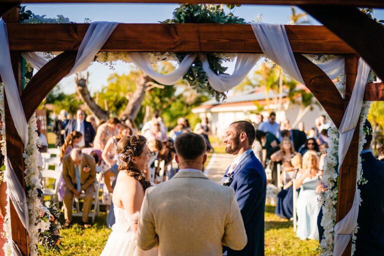 Bride and groom exchanging vows under a wooden arbor at a backyard wedding in Englewood FL