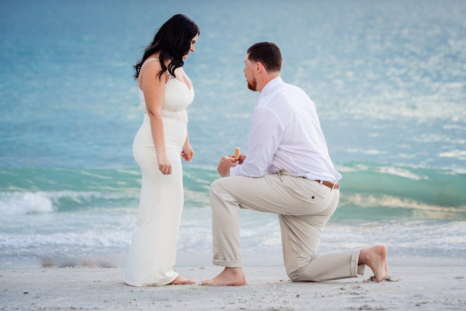 Man kneeling on the beach presenting a ring box to his girlfriend at sunset