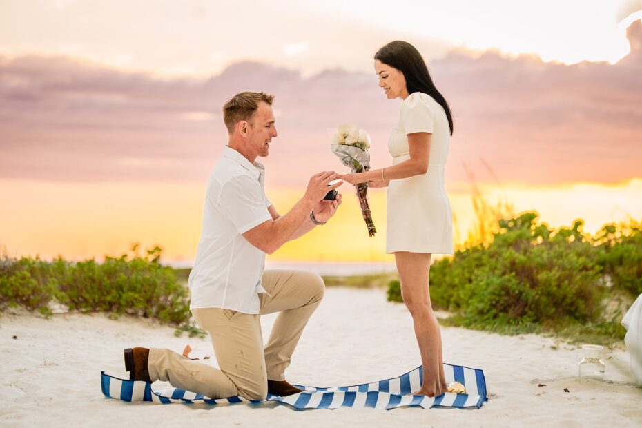 Man on one knee proposing with a ring box while woman holds a bouquet of roses