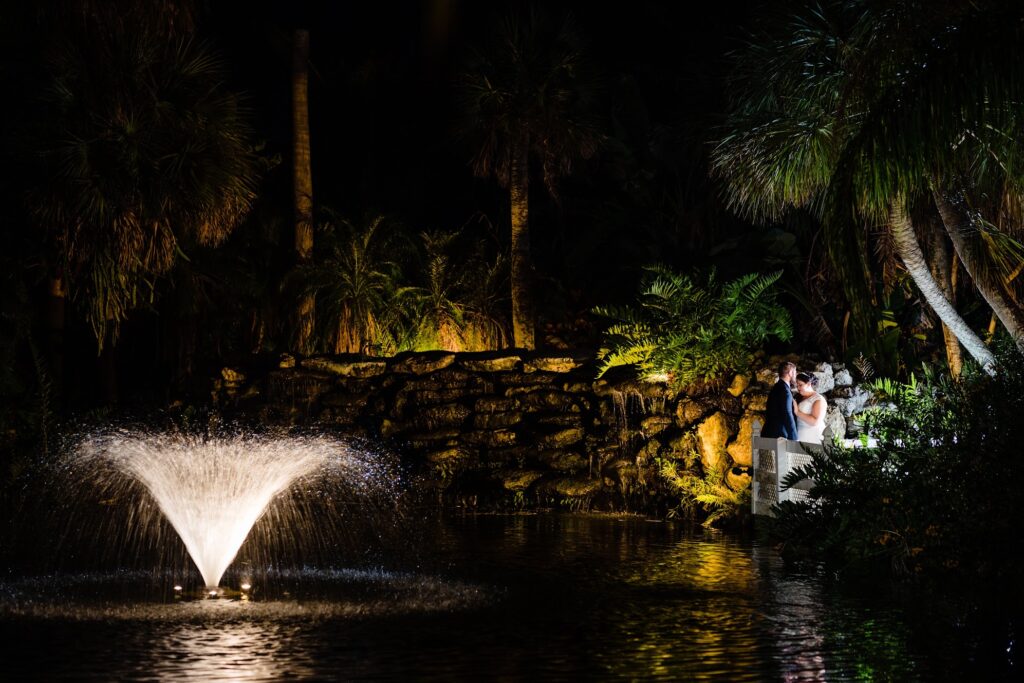 Bride and groom by the lit fountain and rock waterfall at the koi pond at The Pavilion at Mixon Farms